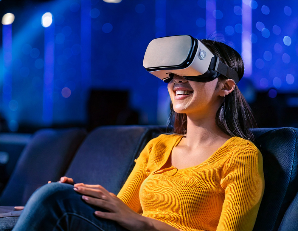 自宅のソファでくつろぎながらVRゴーグルを装着し、笑顔を浮かべる若い女性